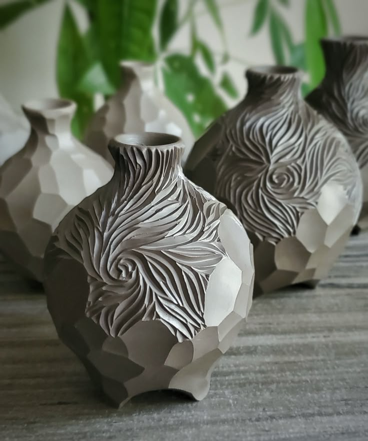 three vases sitting next to each other on top of a wooden table with plants in the background