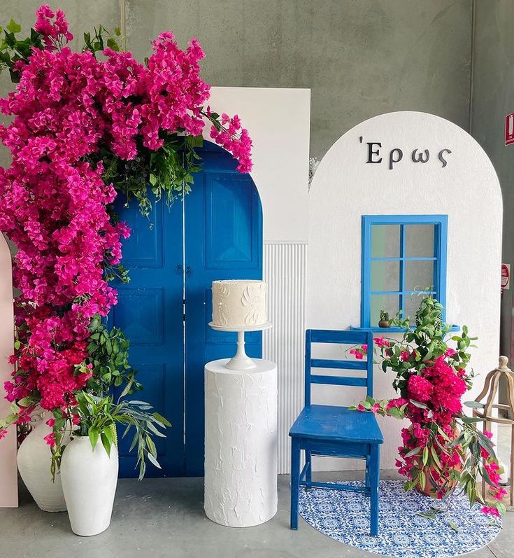 a blue chair sitting in front of a white building with pink flowers growing out of it