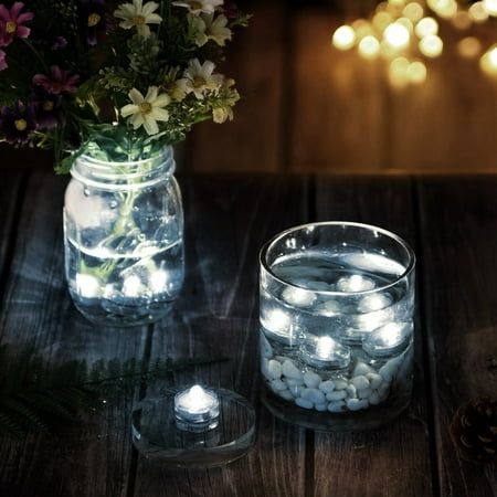 two mason jars filled with rocks and flowers on a wooden table next to a lit candle