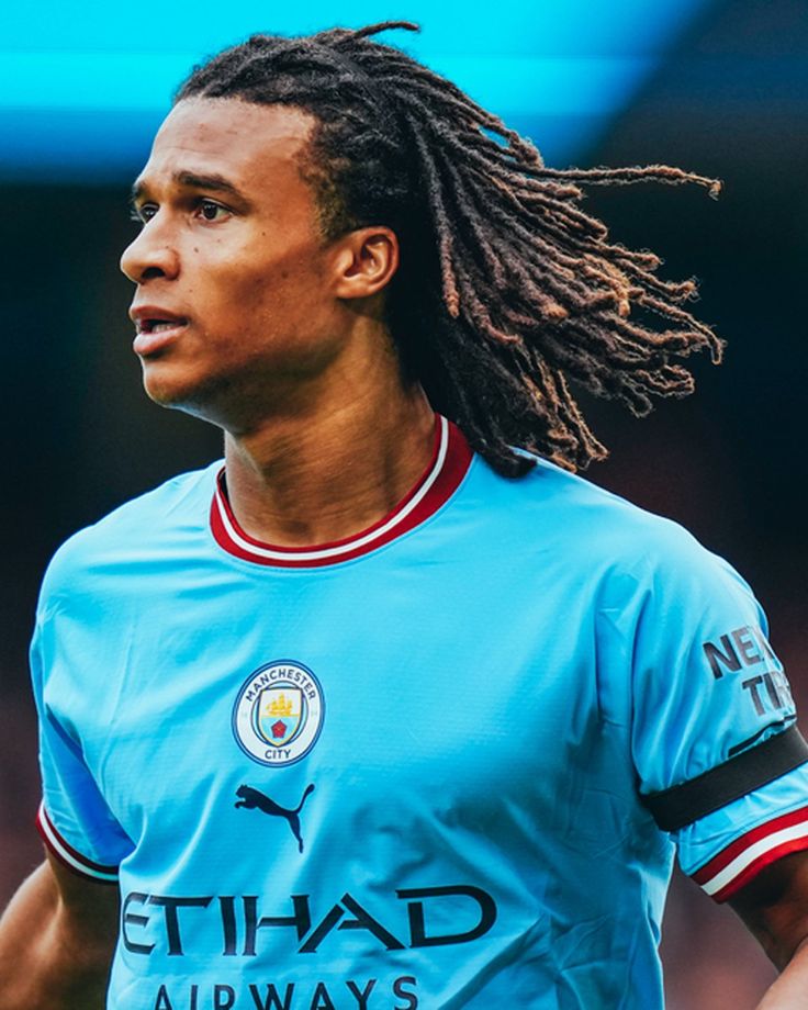 a man with dreadlocks on his head in a blue soccer jersey looking off to the side