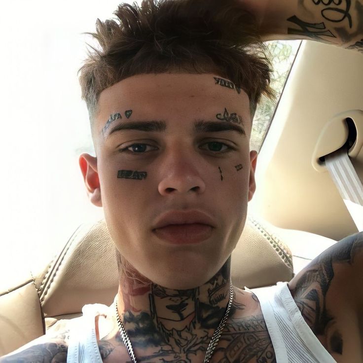 a young man with tattoos on his face and neck sitting in a car looking at the camera