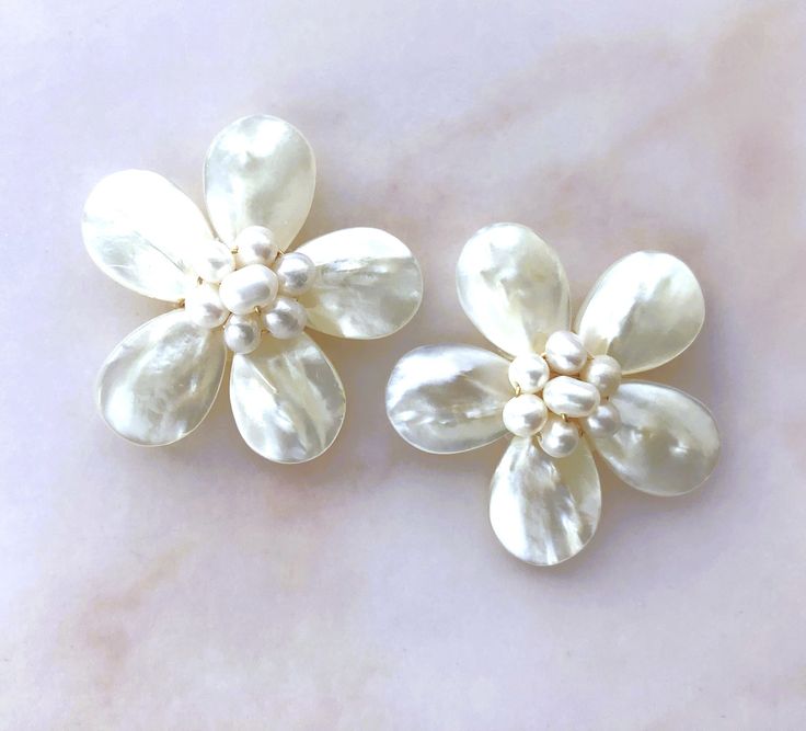 two white flower shaped brooches sitting on top of a marble surface with pearls