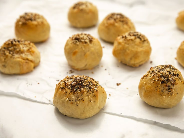 rolls with sesame sprinkled on them sitting on a piece of parchment paper