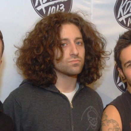 three men standing next to each other in front of a wall