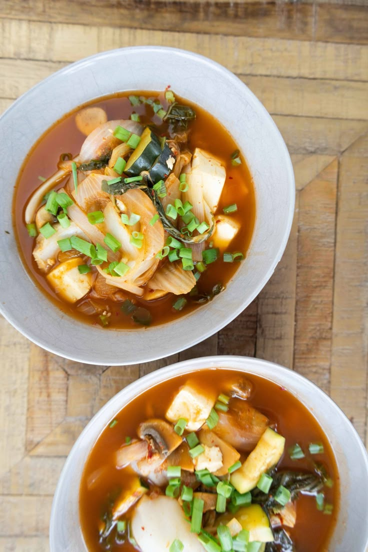 two white bowls filled with food on top of a wooden table