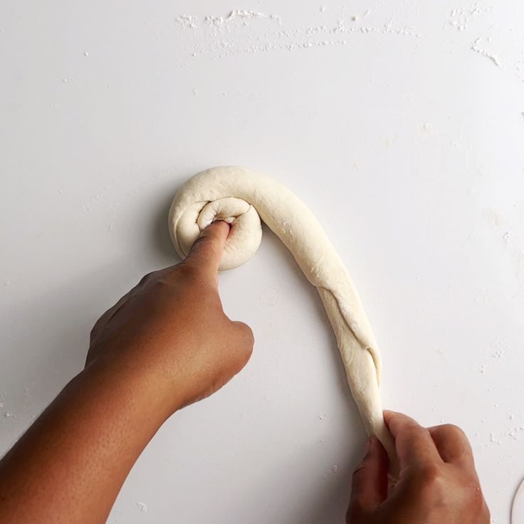 a person is kneading dough on a white surface with their hand in the air