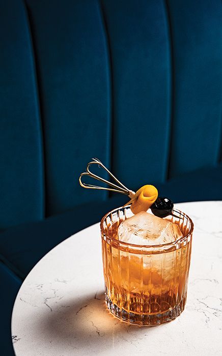 an empty glass sitting on top of a white table next to a blue velvet chair