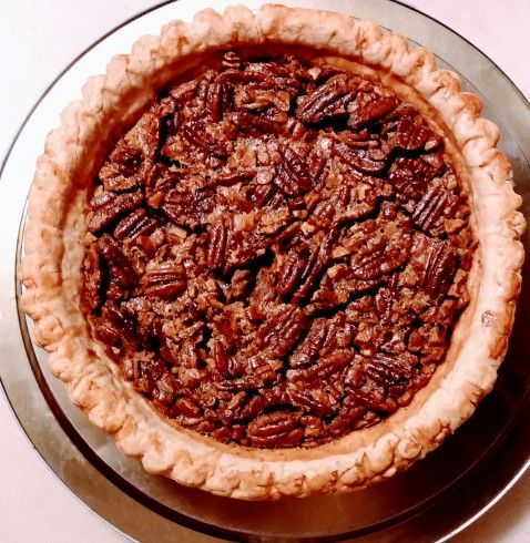 a pecan pie sitting on top of a metal plate next to a white table