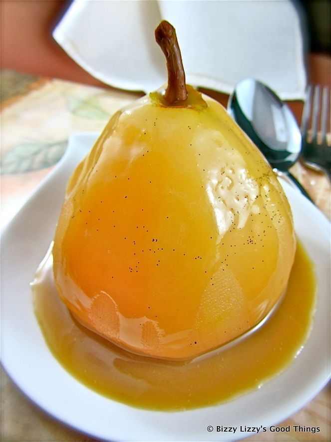 a pear covered in caramel sauce on a white plate with spoons and utensils