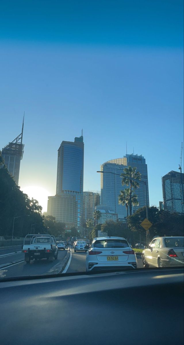 cars are driving down the road in front of tall buildings and palm trees at sunset