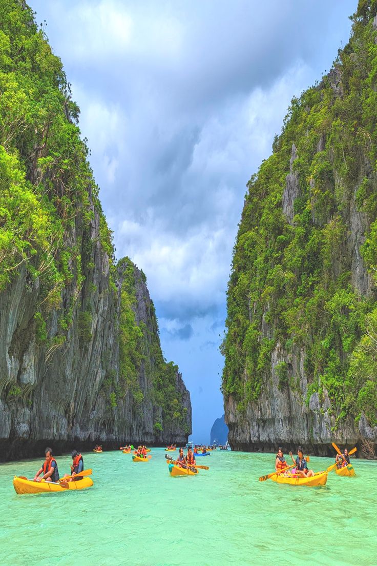 several people in kayaks paddling through the water near cliffs and green trees on either side