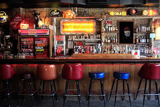 several stools are lined up in front of a bar with neon signs on the wall