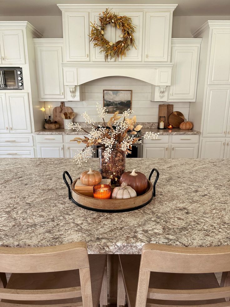 a kitchen with white cabinets and marble countertops, an island with chairs and a centerpiece in the middle