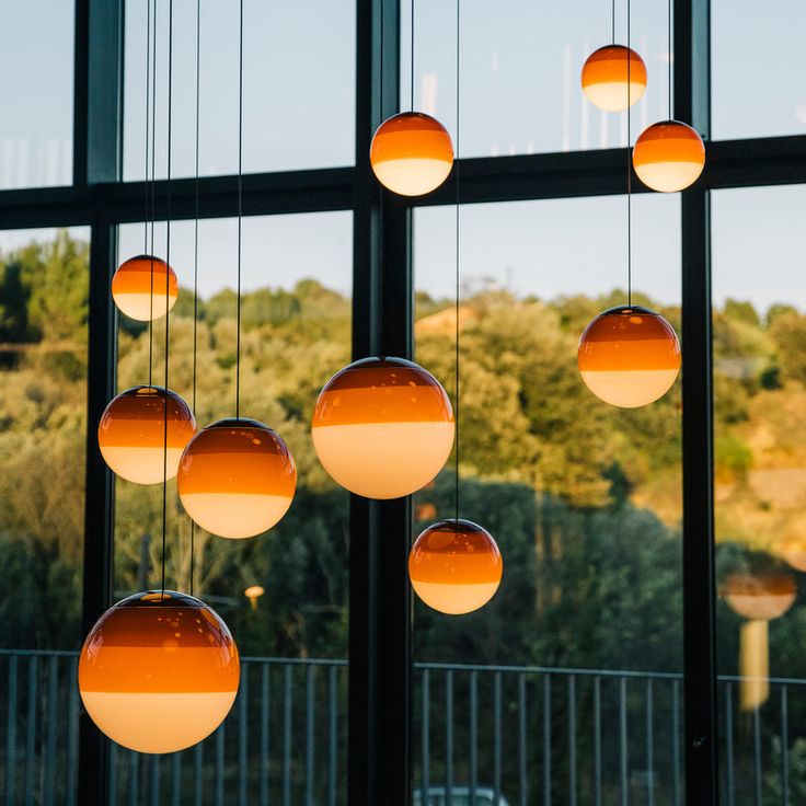 several orange balls hanging from the ceiling in front of a large window with trees outside