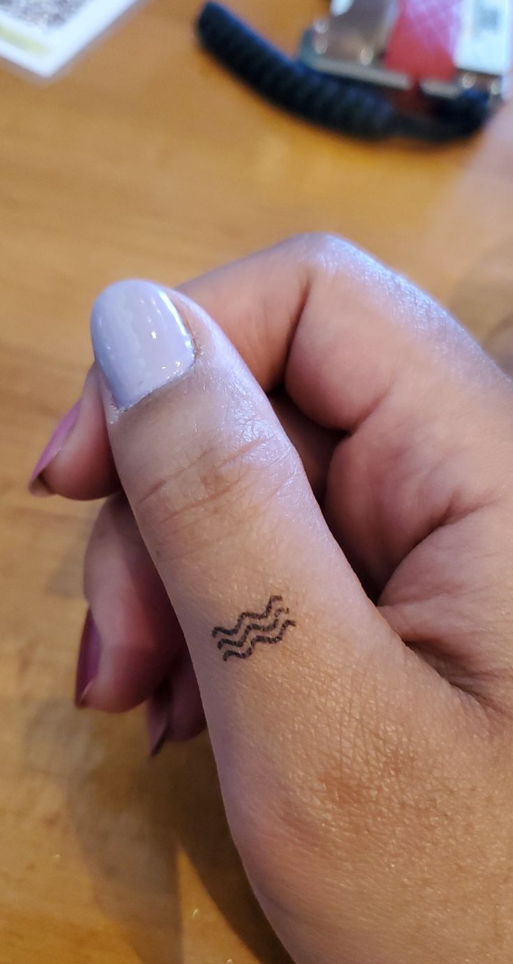 a woman's left hand with a small wave tattoo on her thumb and finger