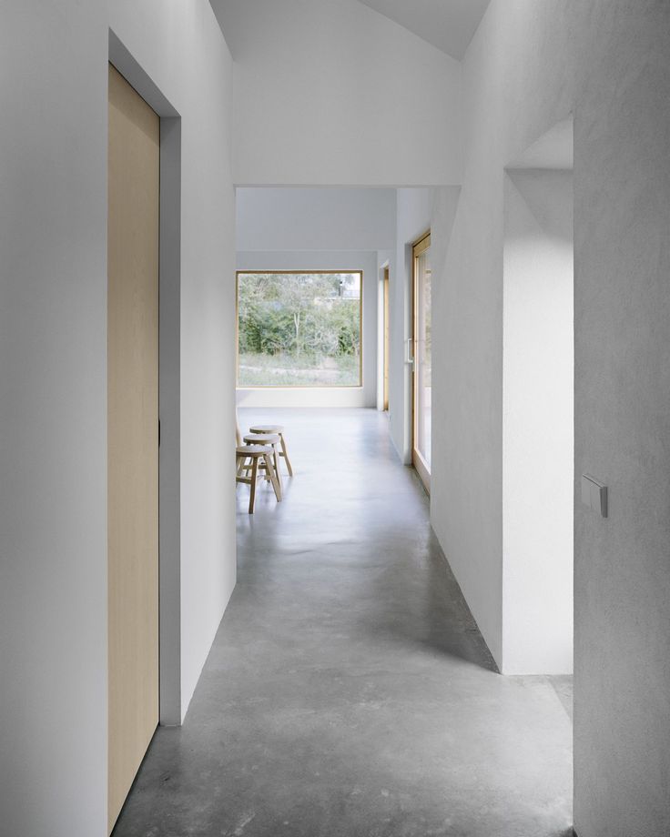 an empty hallway with wooden doors leading to another room that has white walls and concrete flooring