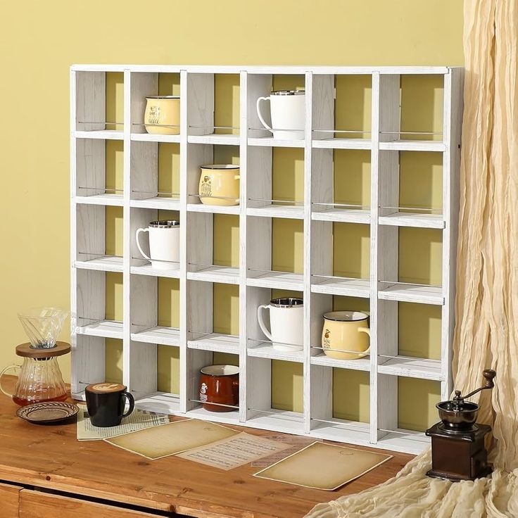 a book shelf with cups on it next to a rug and coffee mugs in front of the bookshelf