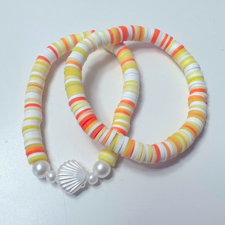 two bracelets with shells and pearls are on a white surface, one has an orange stripe