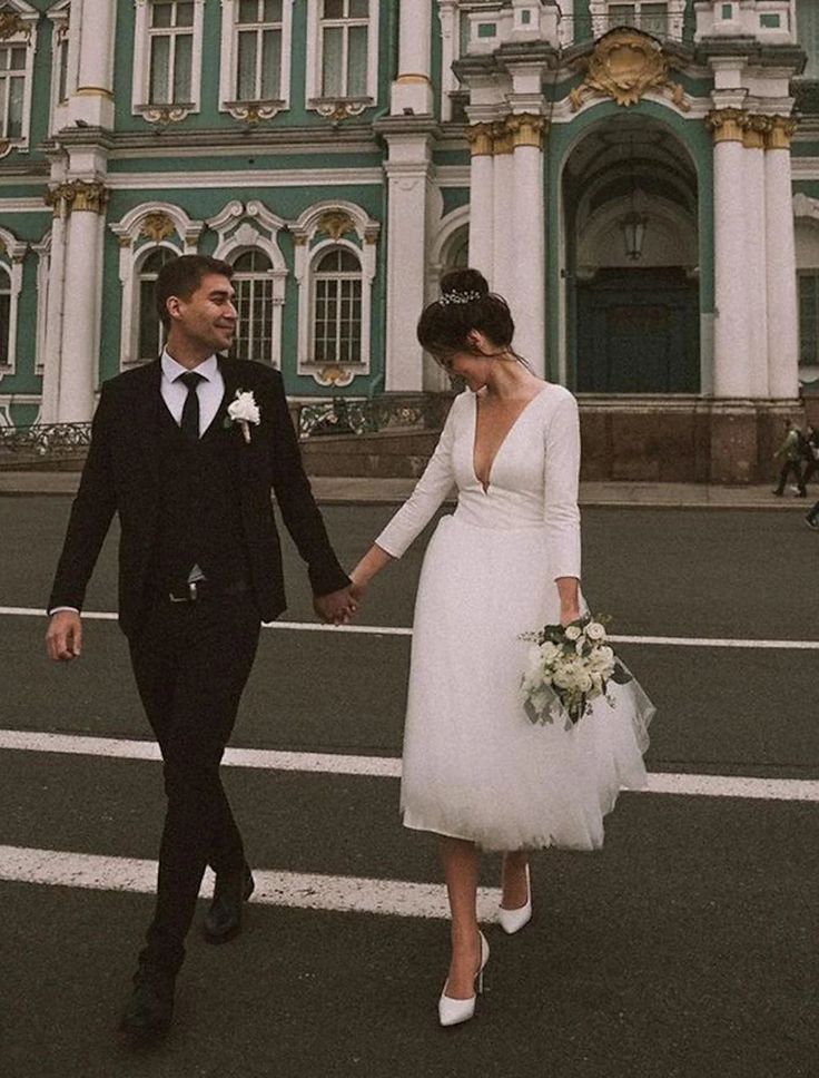 a bride and groom are walking in front of a large green building with white trim