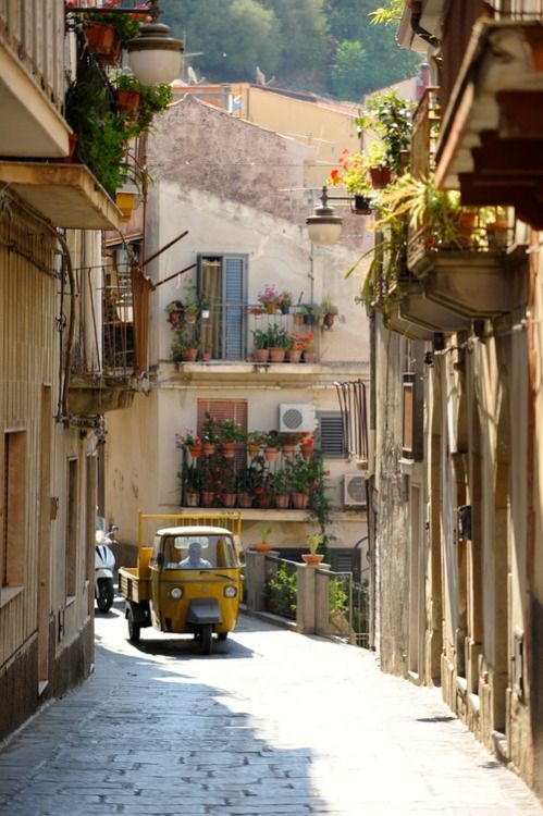 an old yellow car parked on the side of a narrow street in front of buildings