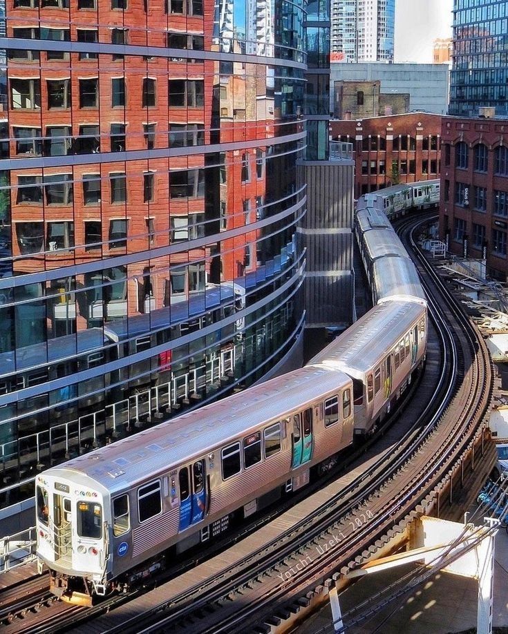 a silver train traveling through a city next to tall buildings