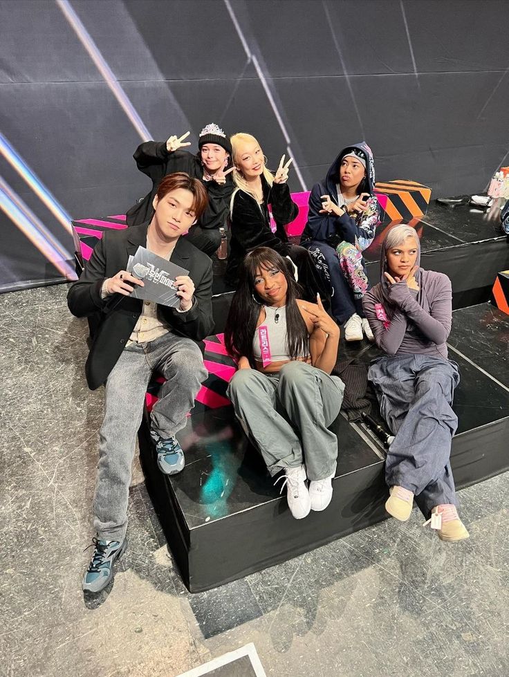 a group of young people sitting on top of a black bench in front of a stage