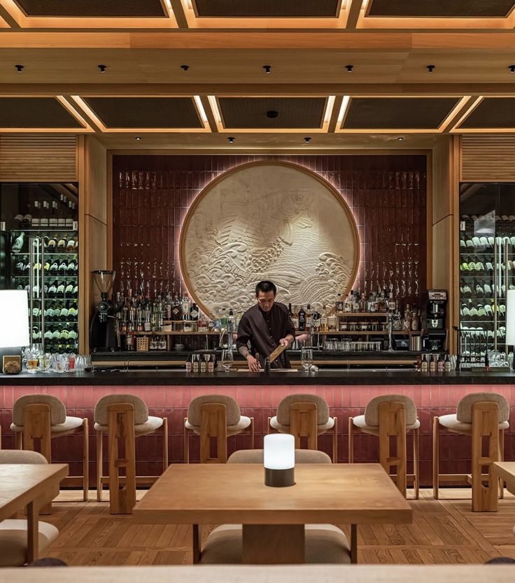 a man behind the bar in a restaurant with wooden tables and stools, bottles on the wall