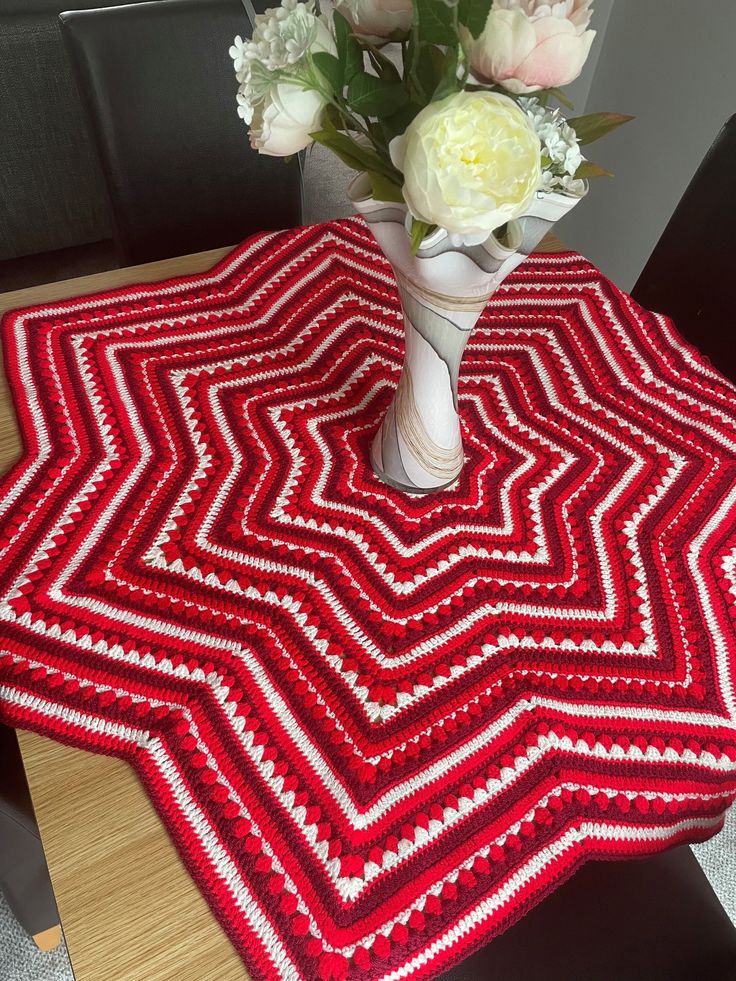 a crocheted table runner with white flowers in a vase on a wooden table