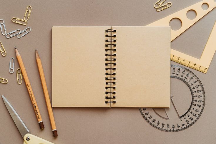 an open notebook sitting on top of a table next to scissors and paper clips with pencils