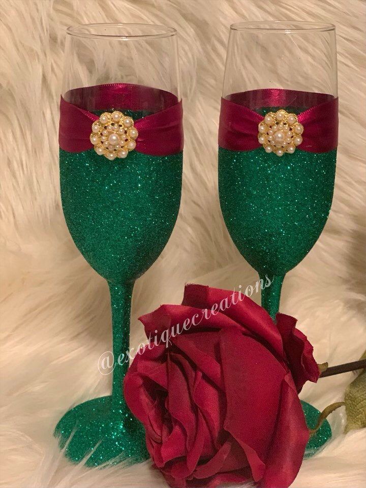 two wine glasses decorated with red and green glitter, one has a rose on it