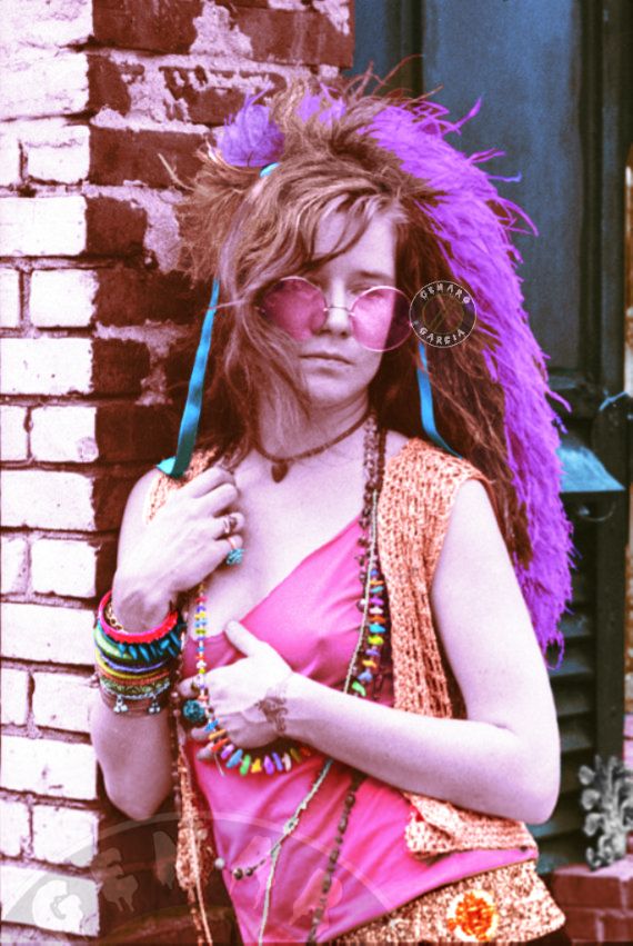 a woman with purple hair and glasses is standing in front of a brick wall holding her hand on her hip