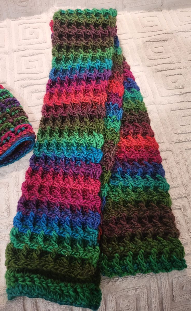 a multicolored crocheted scarf and hat laying on a bed