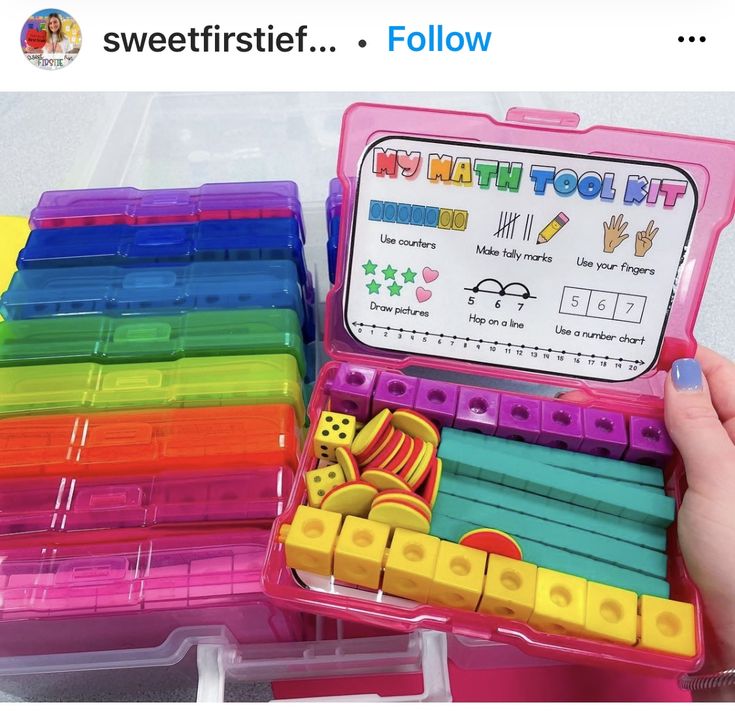 a child's hand holding a pink plastic box filled with lots of colorful toys