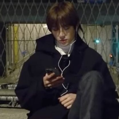 a young man sitting on the ground looking at his cell phone while wearing headphones