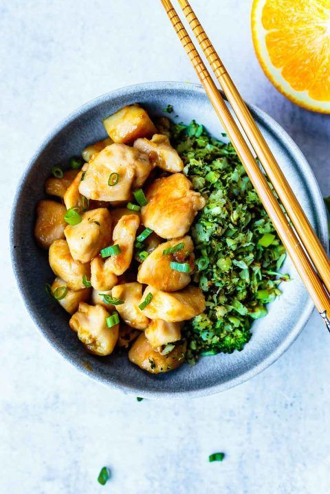 a bowl filled with chicken and broccoli next to chopsticks