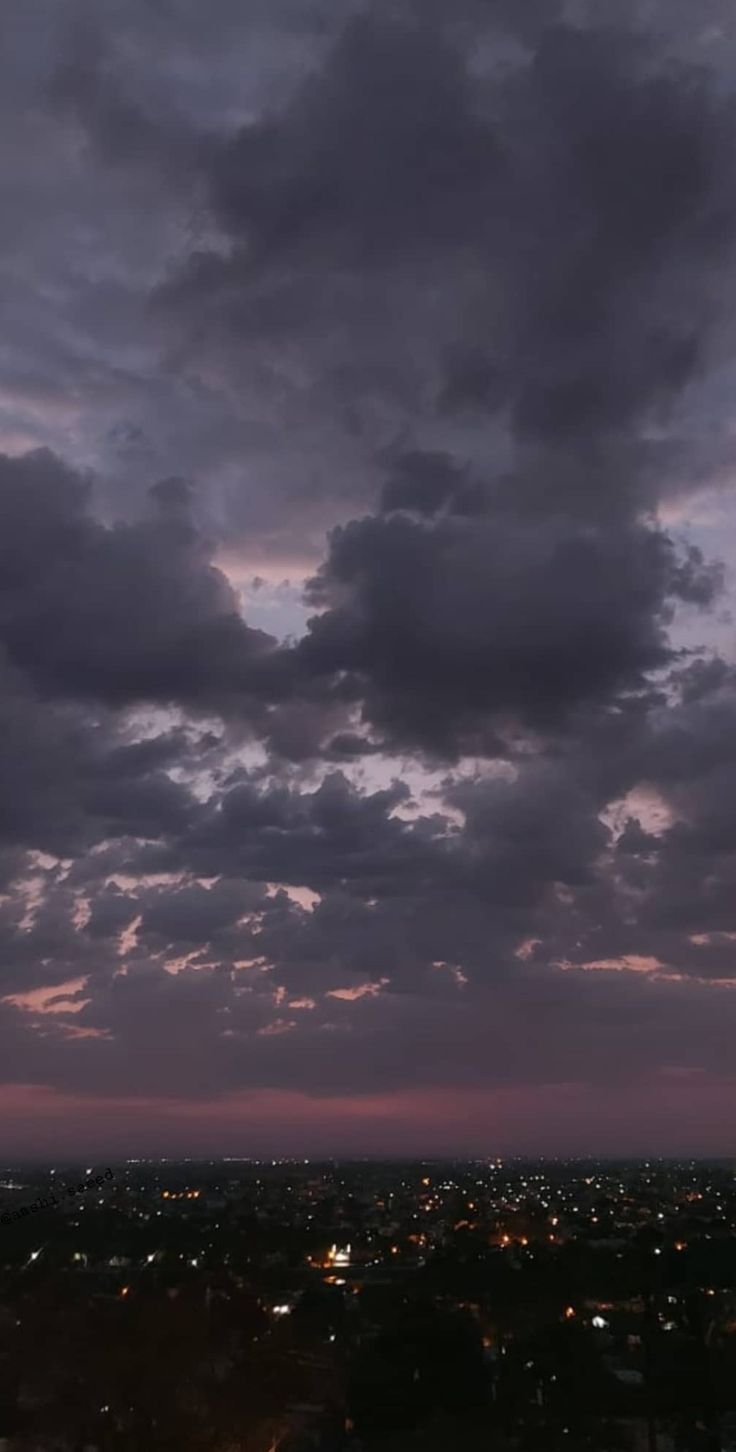 an airplane is flying in the sky at night with dark clouds above it and buildings below