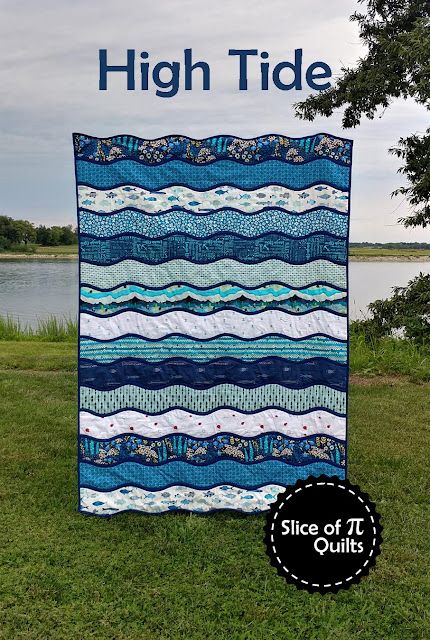 a blue and white quilt sitting on top of a lush green field next to a lake