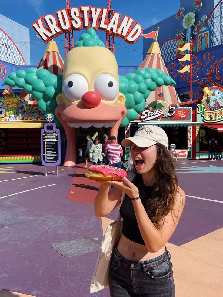 a woman holding a donut in front of a cartoon character at an amusement park