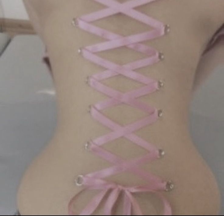 the back of a woman's body with pink ribbon tied around her neck and two pairs of metal studs on each side