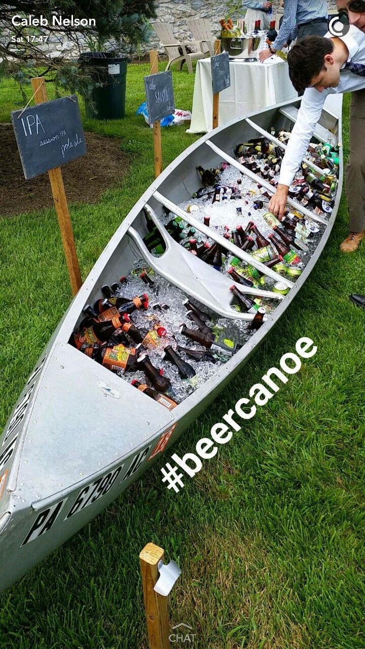 a man standing next to a canoe filled with beer bottles on top of green grass