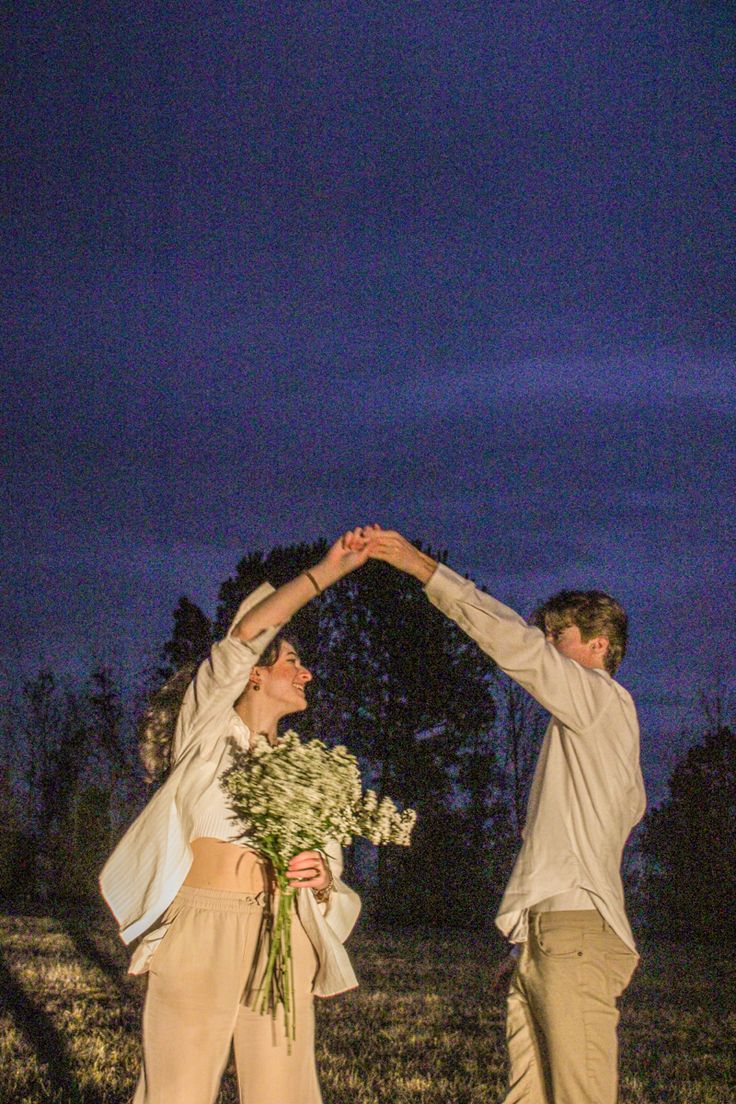 a man and woman standing next to each other with their hands in the air holding flowers