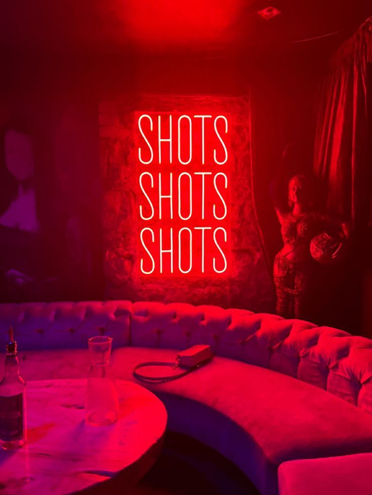 a couch and table in a room with neon lights that read shotshots shot's