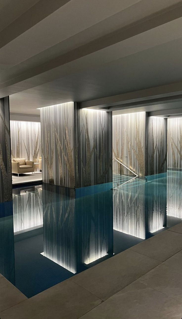 an indoor swimming pool with glass walls and water features at the end, surrounded by concrete flooring