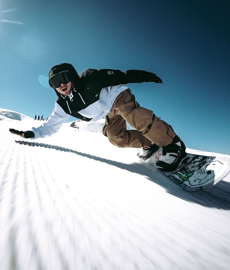 a man riding a snowboard down the side of a snow covered slope on a sunny day