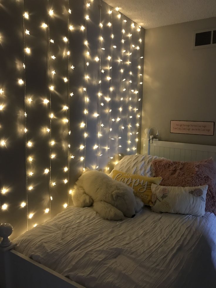 a white bed topped with lots of lights next to a wall covered in string lights