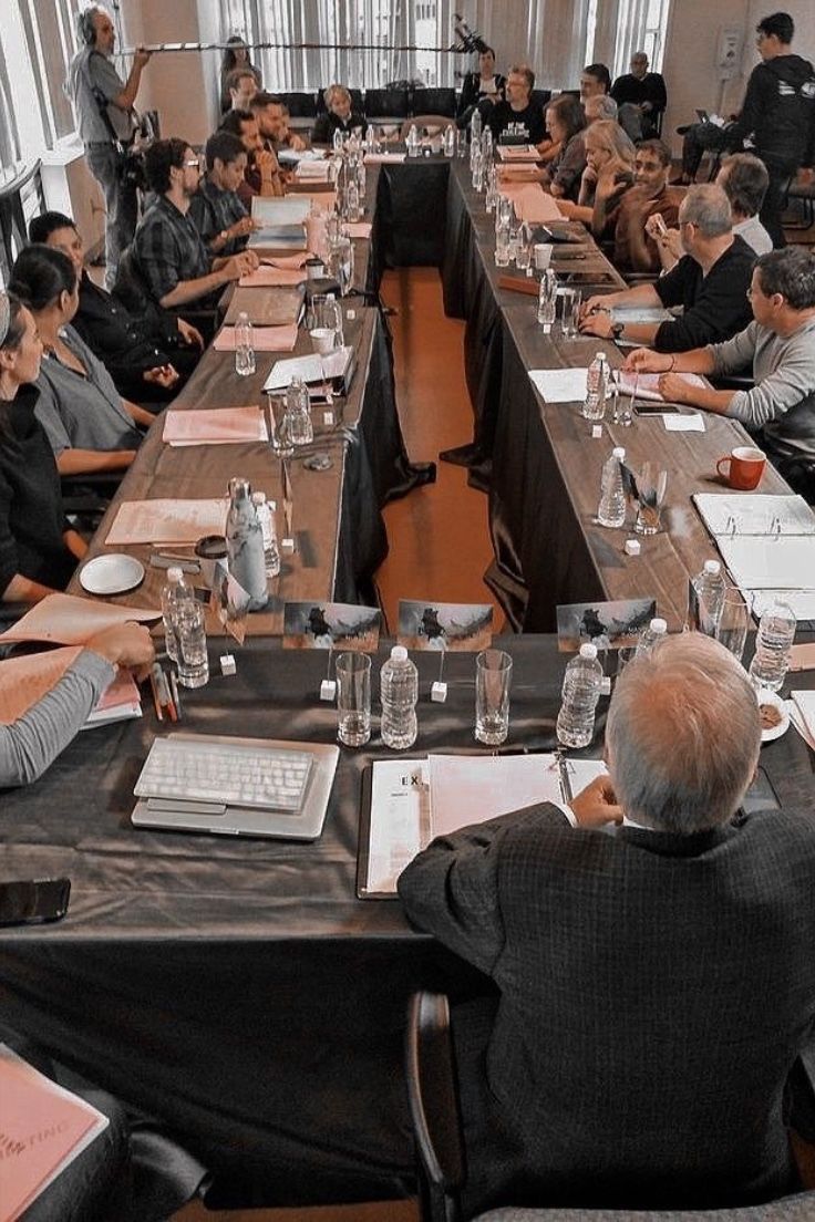 a group of people sitting at long tables with papers and laptops on top of them