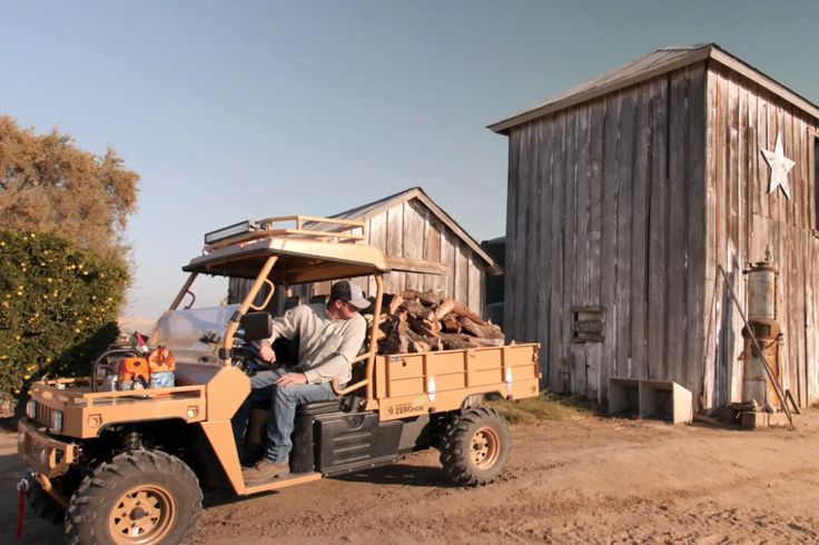 a man riding on the back of a green utility vehicle next to a wooden building