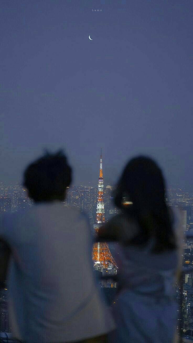 two people are looking at the view from top of a building with a moon in the sky