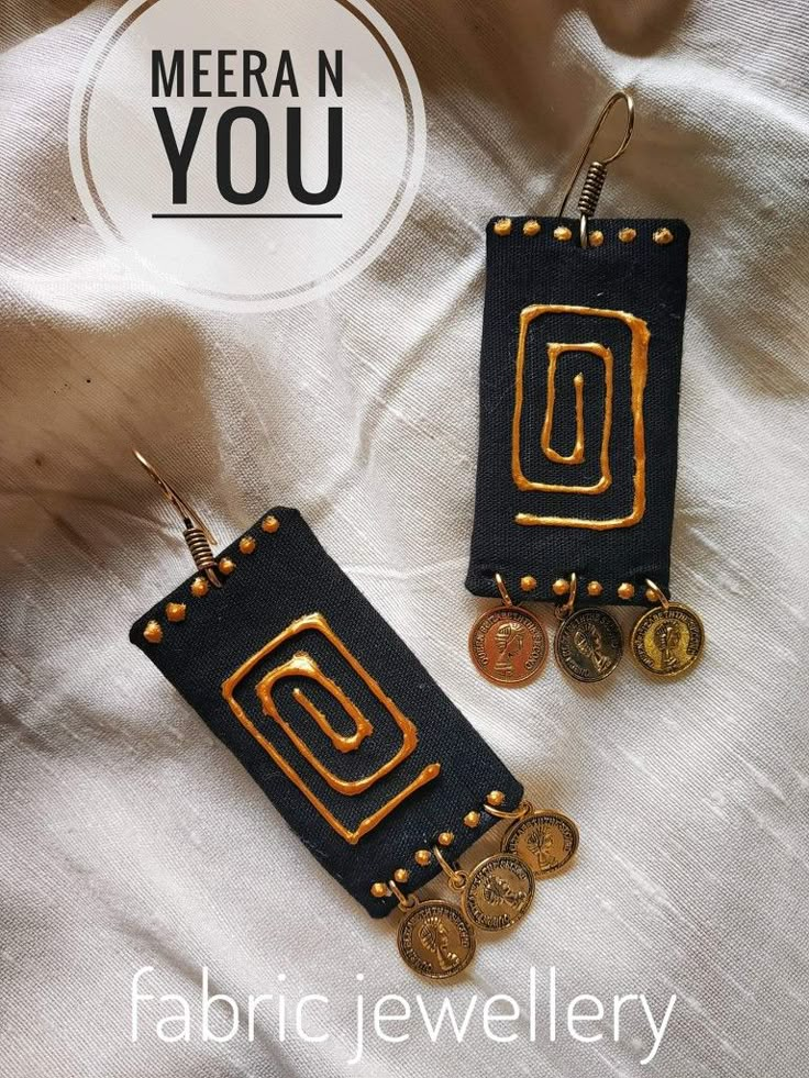 two black and gold earrings with coins hanging from the bottom, on top of a white sheet