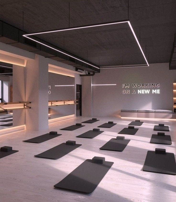 an empty gym with rows of yoga mats on the floor in front of windows and lights above them